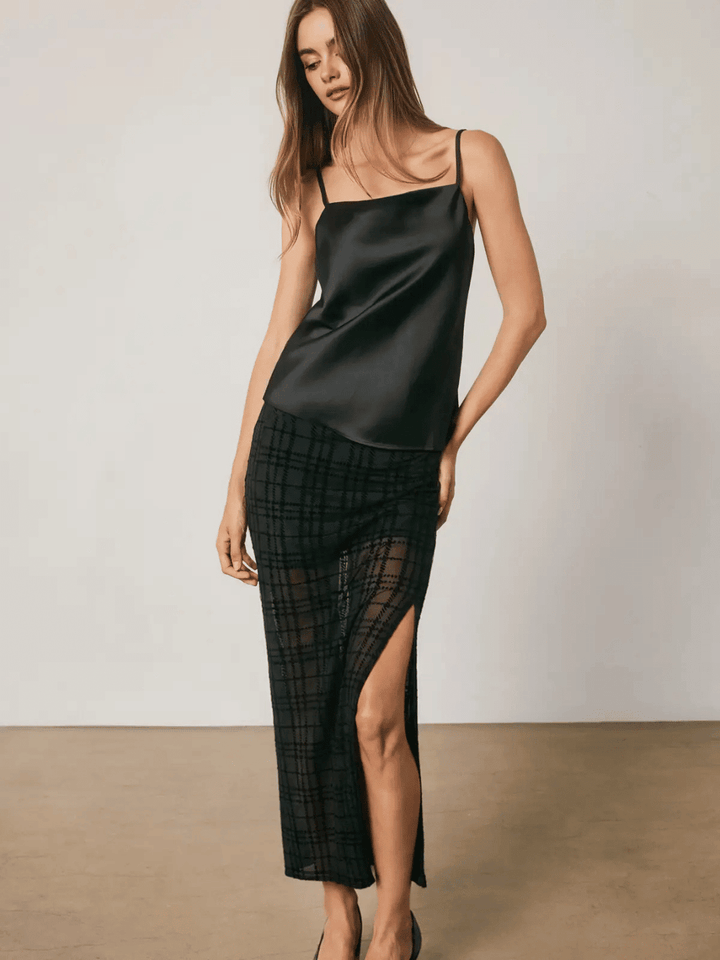 Black satin cami top with square neckline and adjustable straps paired with plaid wrap skirt featuring side slit.