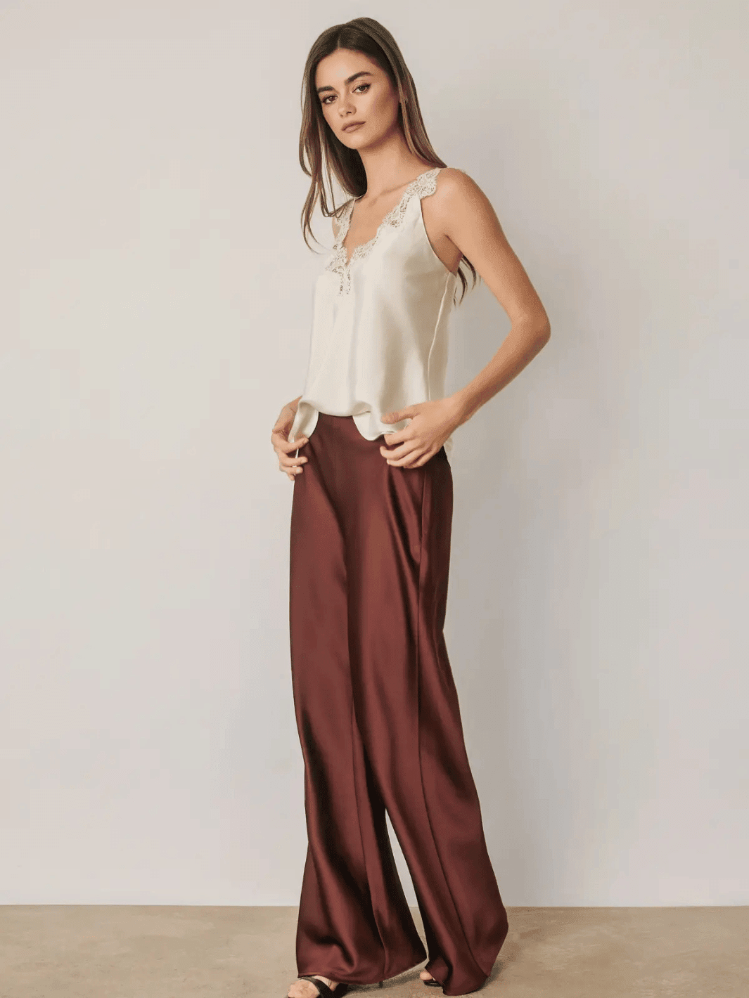 Women wearing burgundy high-rise satin straight leg pants paired with a white lace camisole top.